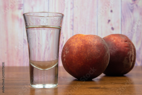 Transparent peach liqueur in a glass and two peaches on a wooden table