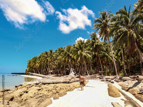 Man walking on the white beach and turquoise water with clear blue sky and lots of palm trees  on Sicsican Island in Balabac, Palawan, Philippines photo