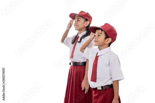 indonesian elementary student wearing uniform giving salute while indonesia flag being raised
