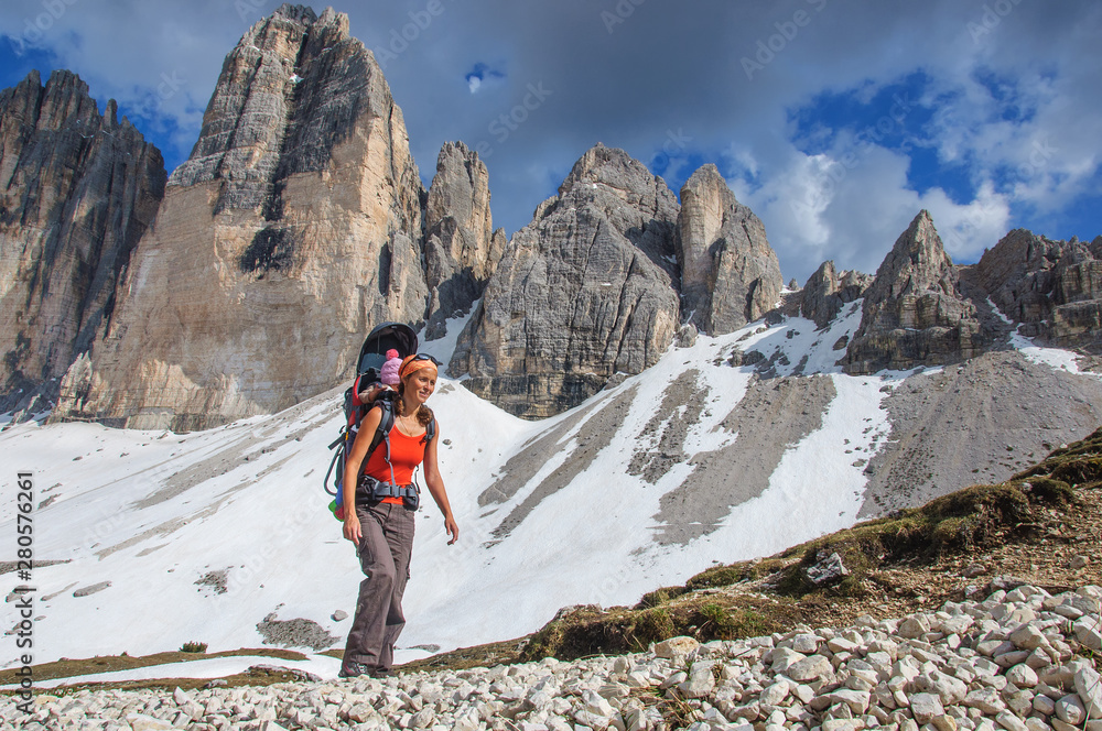 Mum with small child in a backpack walks along dolomites, Italy.