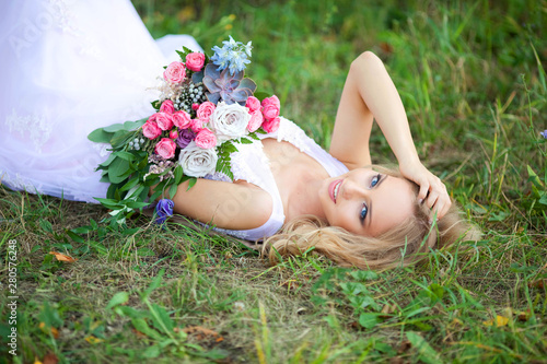 beautiful young woman with make-up in a pink dress lies in the park on the grass with a bouquet of flowers