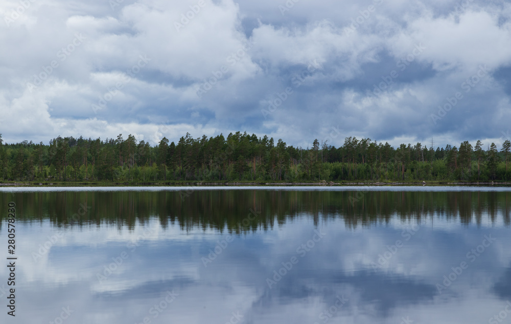 Rainclouds over a Swedish lake inside a forest with the water creating a mirror reflection in the water of the clouds and trees. 