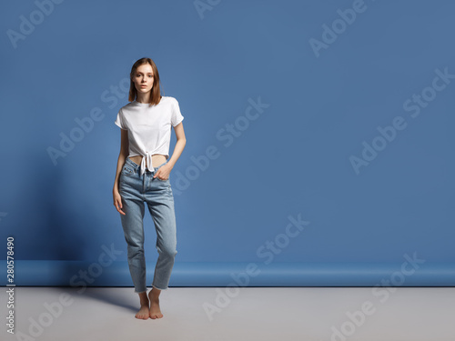 Portrait of the young modern woman. The serious beautiful thin brunette with equal hair in youth clothes. Blue background