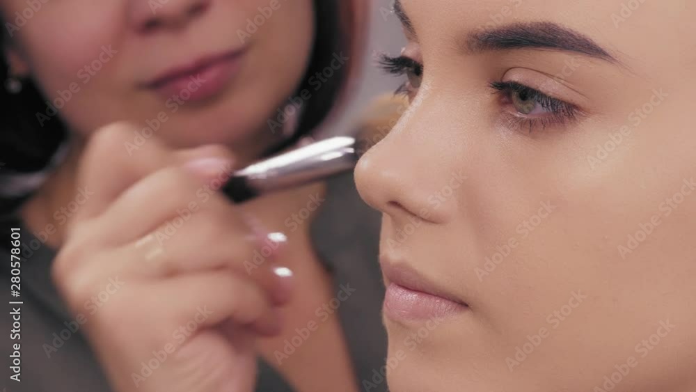 Professional make-up artist makes make-up to a beautiful girl model, feathering powder, highlighter, foundation cream with a special brush for makeup Professional make-up artist makes make-up to a beautiful girl model, feathering powder, highlighter, foundation cream with a special brush for makeup