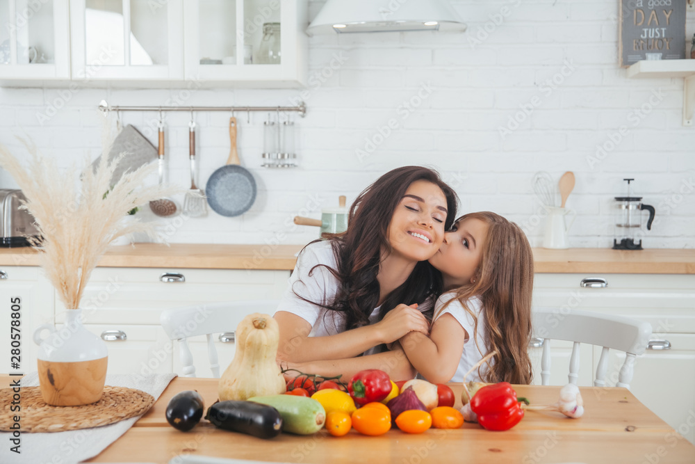 Smiling mom and daughter cooking fruits and vegetables in the Scandinavian-style kitchen. Healthy food. Happy family