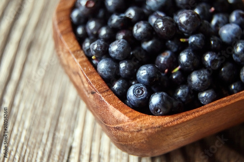 Bilberries in a bowl on brown wooden background, many fresh dark blue berries on table (European blueberries)