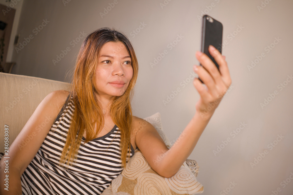lifestyle portrait of young attractive and relaxed 30s Asian Indonesian woman lying comfortable with mobile phone at home living room couch taking selfie portrait photo lifestyle portrait of young attractive and relaxed 30s Asian Indonesian woman lying comfortable with mobile phone at home living room couch taking selfie portrait photo