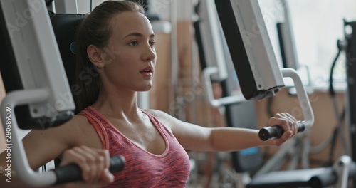 Fit, young woman using chest press machine in gym - slow motion, meduim shot photo