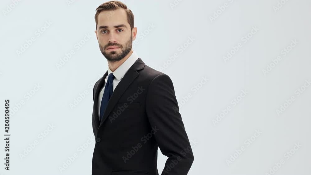 Pensive young businessman in black suit and blue tie raising his head and becoming happy while looking at the camera over gray background isolated Pensive young businessman in black suit and blue tie raising his head and becoming happy while looking at the camera over gray background isolated