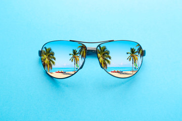 Summer vacation concept. Sunglasses with ocean beach and palms on blue background.