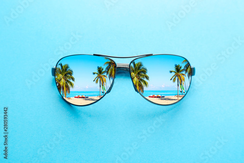 Fototapeta Naklejka Na Ścianę i Meble -  Summer vacation concept. Sunglasses with ocean beach and palms on blue background.