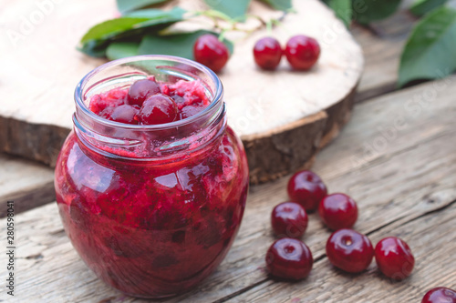 Fresh cherry jelly with fruit on a wooden background near the berries and green leaves.