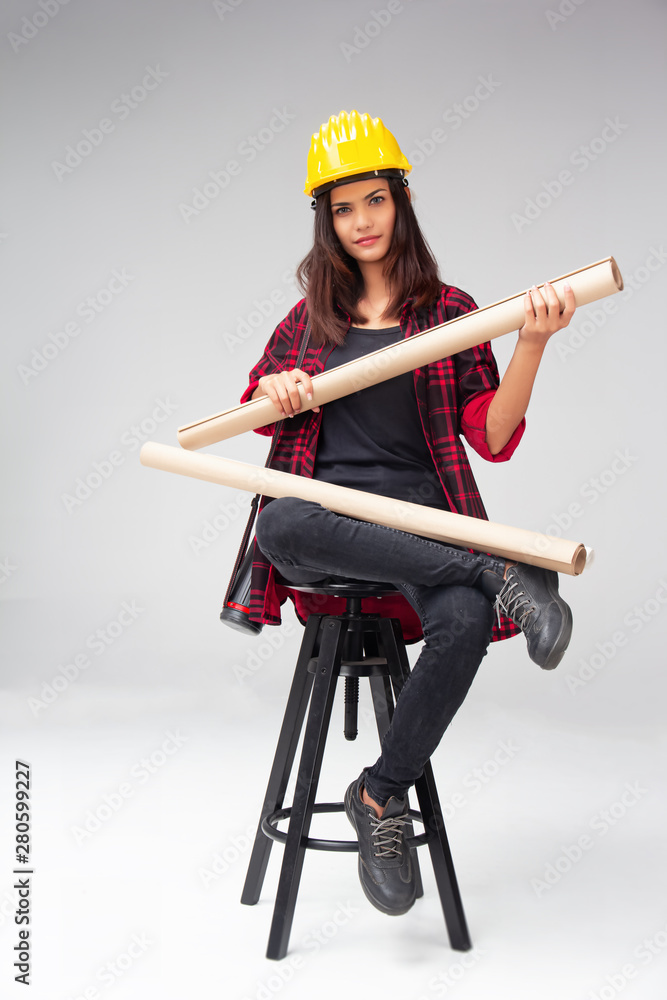 The young woman engineer with yellow safety helmet,sitting on black chair and hold blueprint in her hand,with smart style The young woman engineer with yellow safety helmet,sitting on black chair and hold blueprint in her hand,with smart style