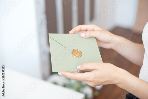 Close-up photo of female hands holding invitation envelope with a wax seal, a gift certificate, a postcard, wedding invitation card