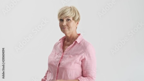 Serious blonde old woman showing bla-bla gesture to someone who is talking too much while looking at the camera over gray background isolated