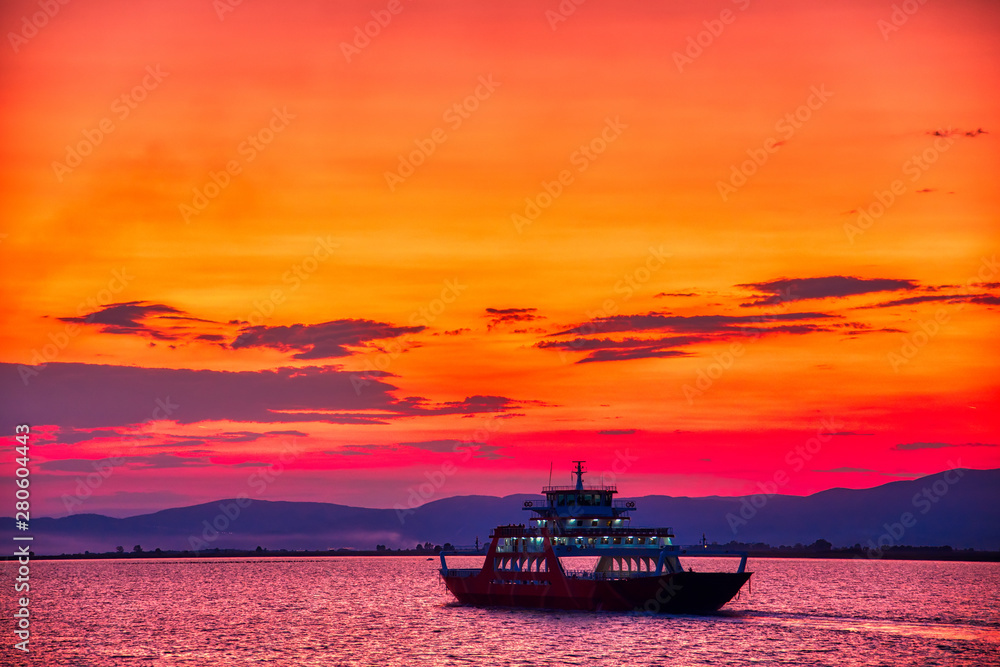 Ferry boat to the sea at sunset in the background of mountains and sun beams, run from Keramoti city to Thassos island in Greece Ferry boat to the sea at sunset in the background of mountains and sun beams, run from Keramoti city to Thassos island in Greece