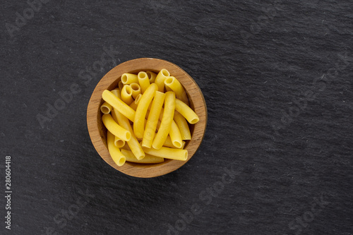 Lot of whole raw pasta macaroni copyspace on right in a wooden bowl flatlay on grey stone
