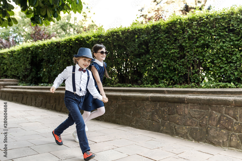 Cute blond guy and cute girl, school year fun time outdoors. Children dressed in school uniform play games in the park Cute blond guy and cute girl, school year fun time outdoors. Children dressed in school uniform play games in the park