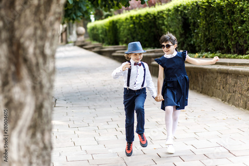 Cute blond guy and cute girl, school year fun time outdoors. Children dressed in school uniform play games in the park