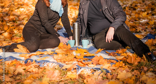 A loving couple - a man and a woman - spend time together in the autumn park, drink tea from a thermos