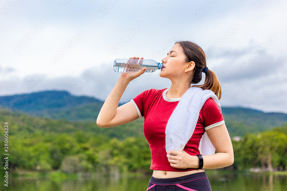 Beautiful Asian athlete woman drinking water during her break from morning exercise at a lake park with view of lake and mountains in the background, healthy lifestyle Beautiful Asian athlete woman drinking water during her break from morning exercise at a lake park with view of lake and mountains in the background, healthy lifestyle