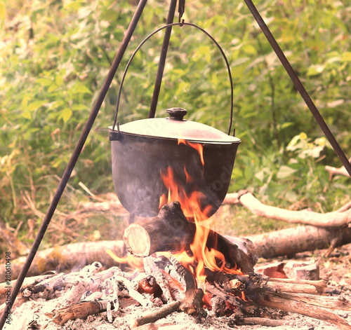 cooking delicious tasty food outdoors on fire in iron pot in summer in good weather with wood from forest