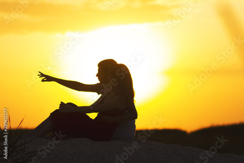 silhouette of a loving couple at sunset sitting on sand on the beach, profile of a man and a woman in love staring ahead at one goal, a romantic scene in nature, summer rest