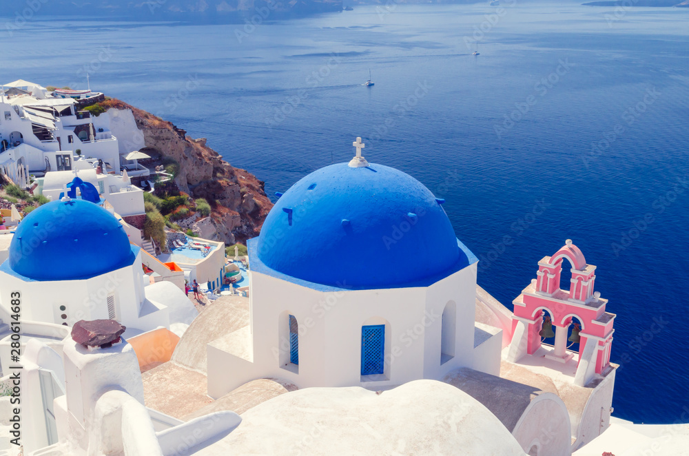 Fototapeta premium Oia Village, Santorini Cyclade islands, Greece. Beautiful view of a blue dome church and a pink towerbell.