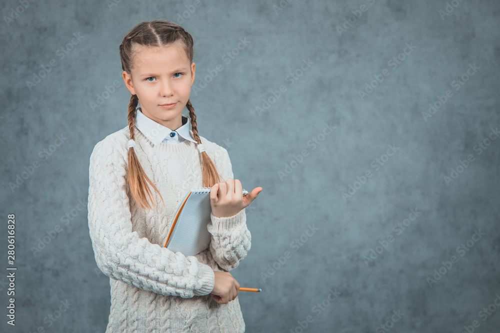The portrait of beautiful blond schoolgirl in studio listening attentively is isolated on grey background. The portrait of beautiful blond schoolgirl in studio listening attentively is isolated on grey background.