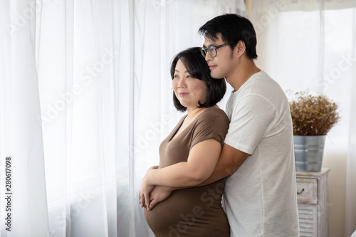 pregnant woman and her husband happy smiling while spending time together in the bedroom on white bed