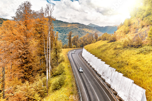 golden autumn mountain landscape with asphalt road and car traffic against beautiful clouds sky background aerial view of orange and yellow forest in fall with scenic mountains scenery