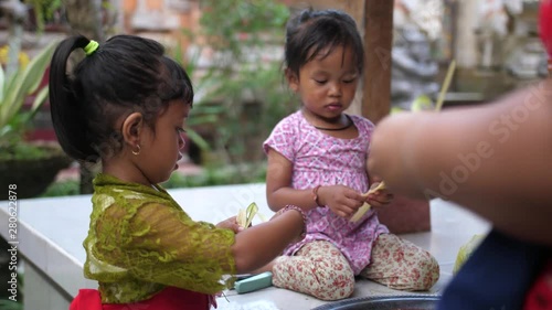 Adorable little girls help mom making crafts from palm leaves that will be sold or used as religious offerings. Balinese kids squabble over a stapler.