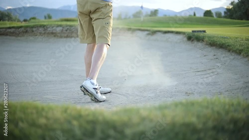 Slow motion shot behind a golfer hitting the golf ball out of the sand trap onto the putting green. The golfer is playing on a nice resort golf course. photo