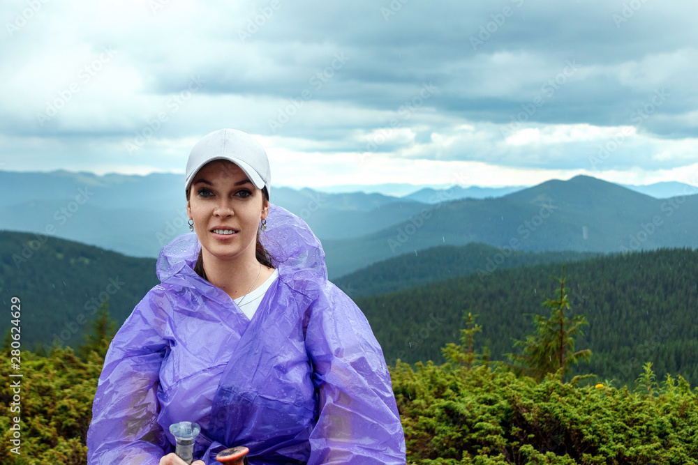 Portrait of a beautiful girl in a raincoat and a white cap against the background of the beautiful Karpatsky mountains. Travel concept, leisure activity, vacation