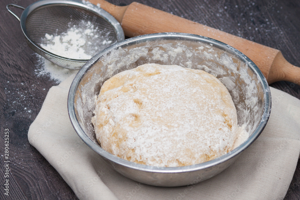 Raw dough with flour and accessories on the dark wooden table.