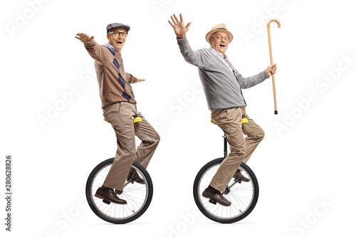 Two cheerful senior men riding unicycles and looking at the camera photo