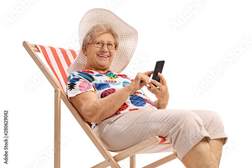 Canvastavla Elderly woman on a vacation with a phone sitting in a deck chair and looking at