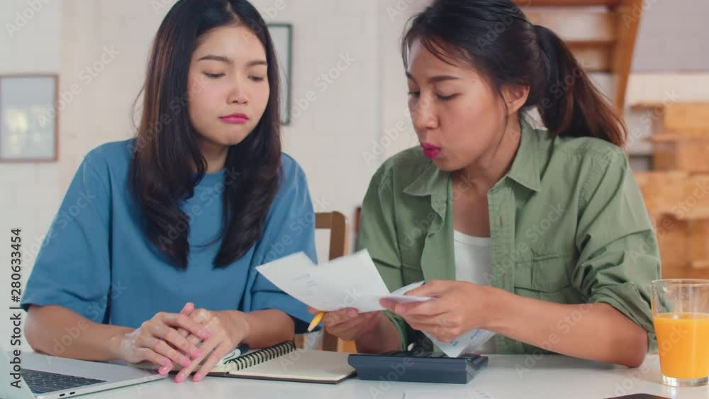 Business Asian Lesbian lgbtq women couple do account at home, Young Asia girl serious, stress while using calculator record budget, tax, financial document on laptop working in kitchen concept. Business Asian Lesbian lgbtq women couple do account at home, Young Asia girl serious, stress while using calculator record budget, tax, financial document on laptop working in kitchen concept.