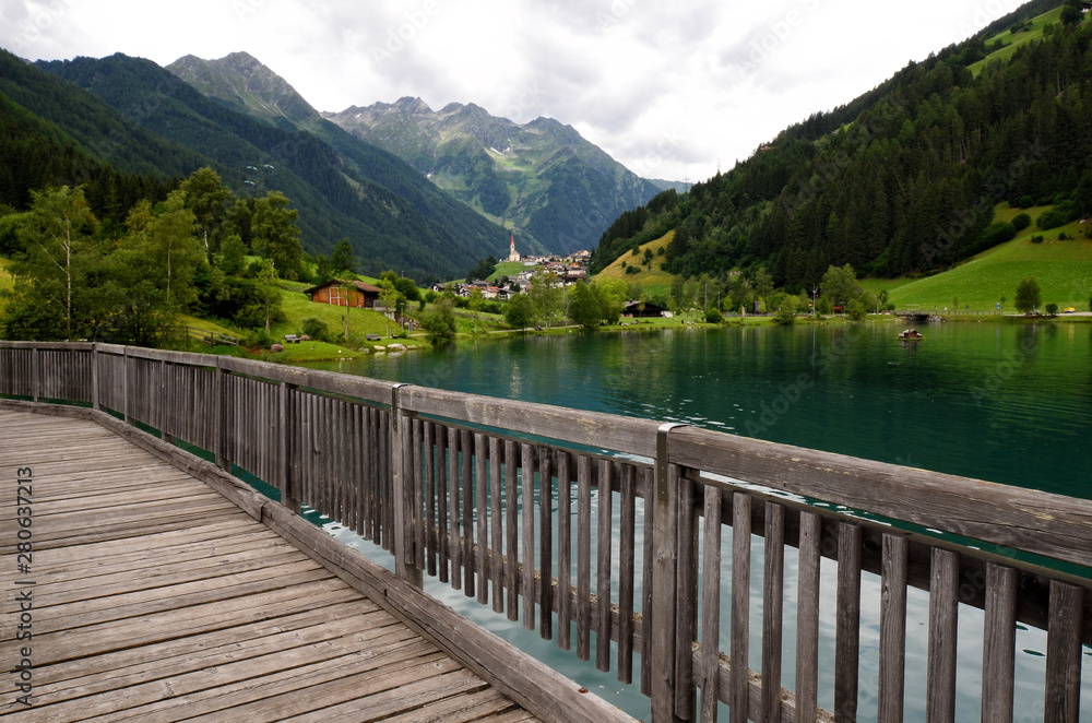 wooden bridge on beautiful lake of Lappago with flowers on foreground, Val Pusteria south tyrol (BZ) Italy
