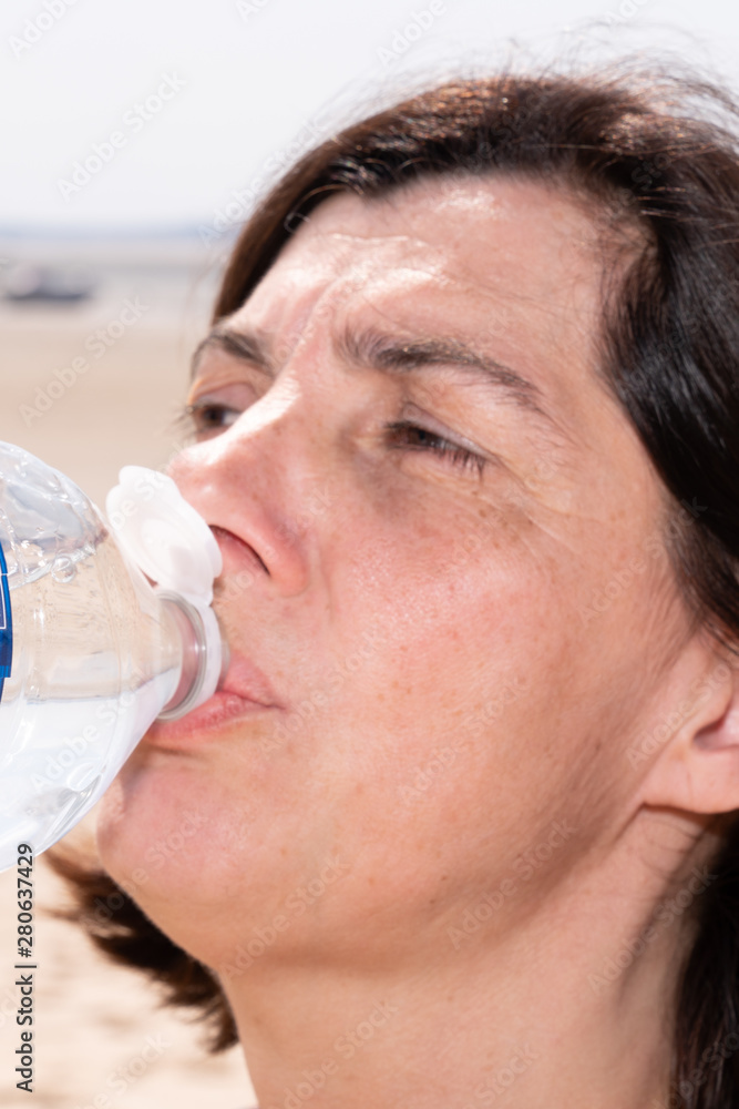 middle aged woman drinking bottle of water on a hot summer day closeup middle aged woman drinking bottle of water on a hot summer day closeup