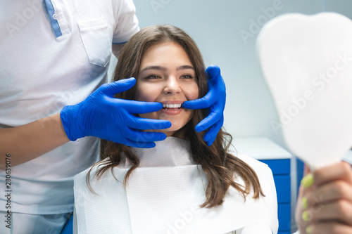 beautiful young brunette woman having examination at dental office while dentist showing whitening results to satisfied patient