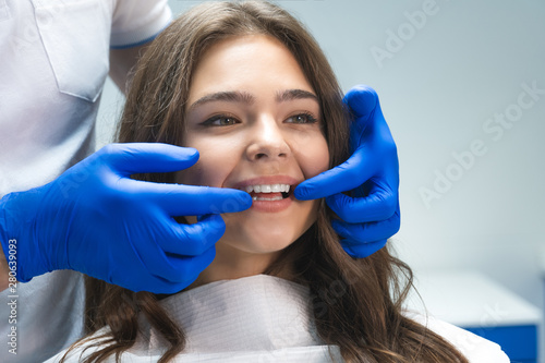 beautiful young brunette woman having examination at dental office while dentist showing whitening results to happy patient