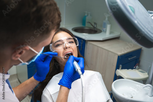 Fototapeta dentist in mask filling the patient's root canal while she is lying on dental ch