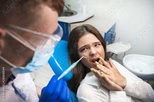 beautiful young scared brunette patient woman having examination at dental office by handsome dentist in mask and blue gloves
