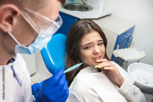 beautiful scared frightened patient woman having examination at dental office by handsome dentist in mask and blue gloves