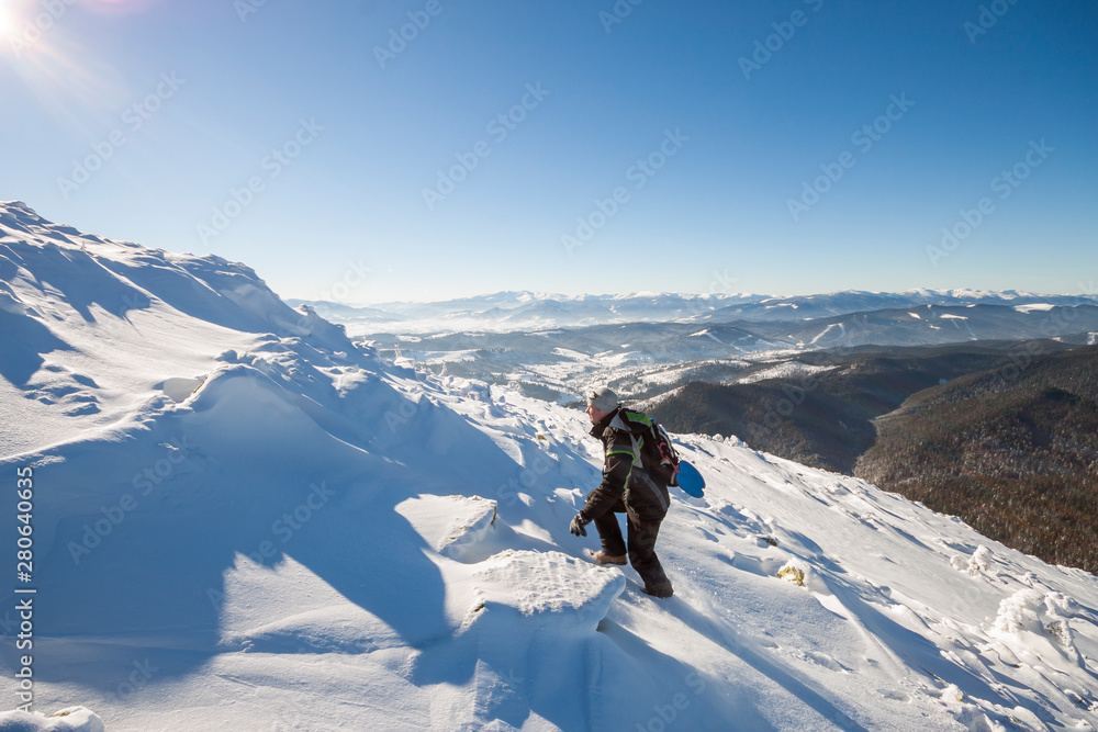 Tourist hiker climber in winter clothing with backpack climbing dangerous rocky steep mountain slope covered with deep snow, white sun rays shining in bright blue sky copy space background.