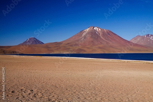 View on deep blue lake at Altiplanic Laguna (Lagoon) Miscanti in Atacama desert with partly snow capped cone of volcano Meniques in the background - Chile photo