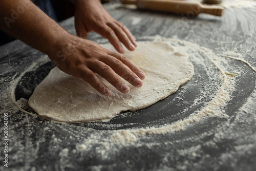 The chef in the kitchen rolls out the pizza dough. Male baker hands