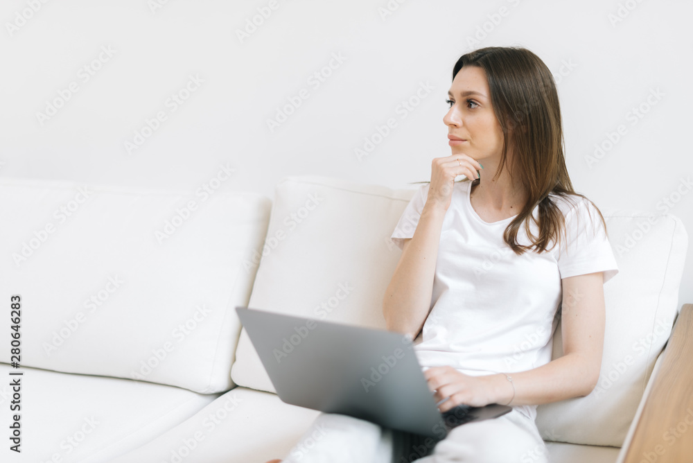 Close-up portrait of wondering girl looking away sitting at couch with laptop Close-up portrait of wondering girl looking away sitting at couch with laptop