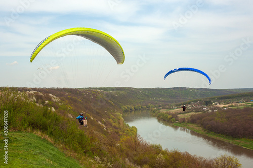 Paragliding over the green field in summer sunny day. Two paragliders fly over green field near Dnister river in Ukraine.